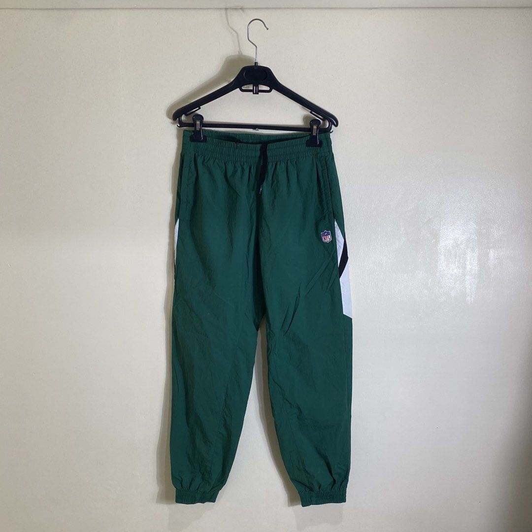 NFL Team Apparel Green Track Pants (Category: Joggers) located in Cebu City. Submitted by theloose.thread (Listing ID 1461781091, Image 1). Description: - Green NFL track pants - White and black side stripes - Elastic waistband with drawstring - NFL logo on right leg - Ideal for casual wear or sports - Made from a polyester and polyurethane blend.