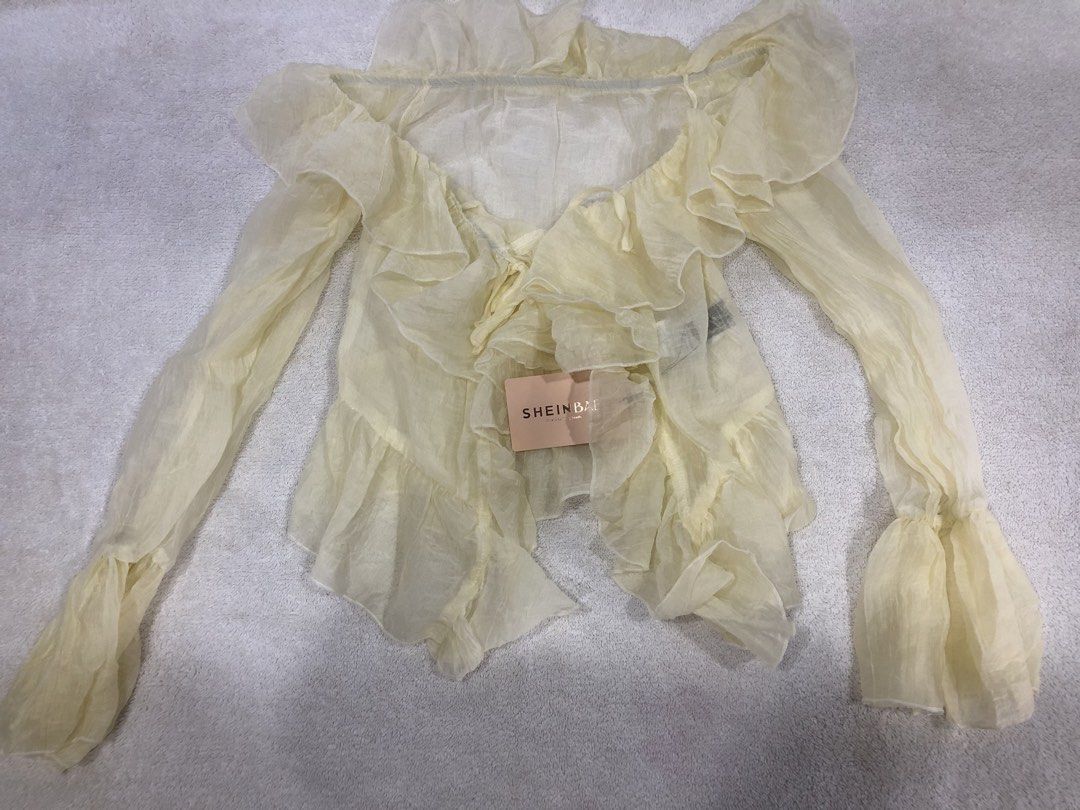 SHEINBAE Sheer Ruffle Long Sleeve Top (Category: Longsleeves) located in Manila. Submitted by janmichael26601 (Listing ID 1461619009, Image 1). Description: - Brand new with tags attached - Cream sheer fabric - Long ruffled sleeves - Tie front closure - Ruffled hemline - Lightweight and flowy material - Ideal for layering or as a standalone statement piece.