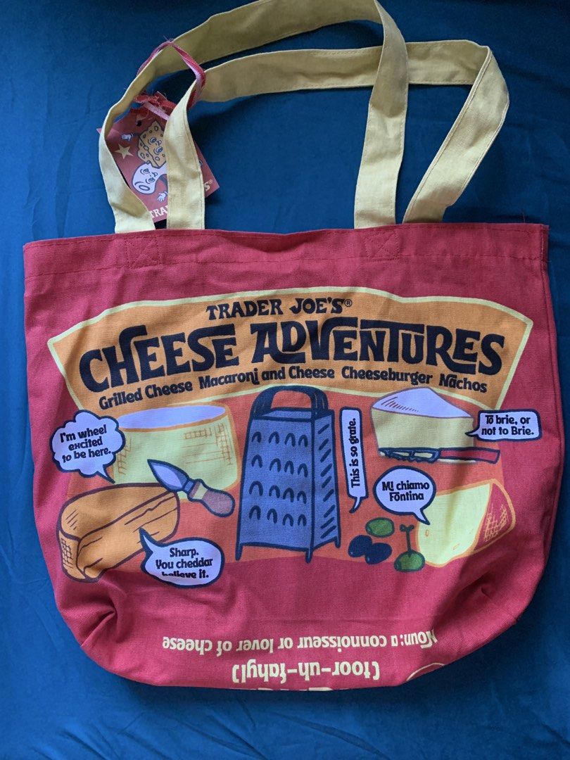 Trader Joe's Cheese Adventures Tote Bag (Category: Tote Bags) located in Paranaque City. Submitted by ashleyreads (Listing ID 1461570587, Image 2). Description: - Trader Joe's tote bag with a fun cheese theme. - Features 'Cheese Adventures' on one side and 'Cheese Experience' on the other. - Vibrant red bag with contrasting yellow straps. - Adorned with illustrations of various cheeses and witty puns. - Ideal for grocery shopping or as a stylish 