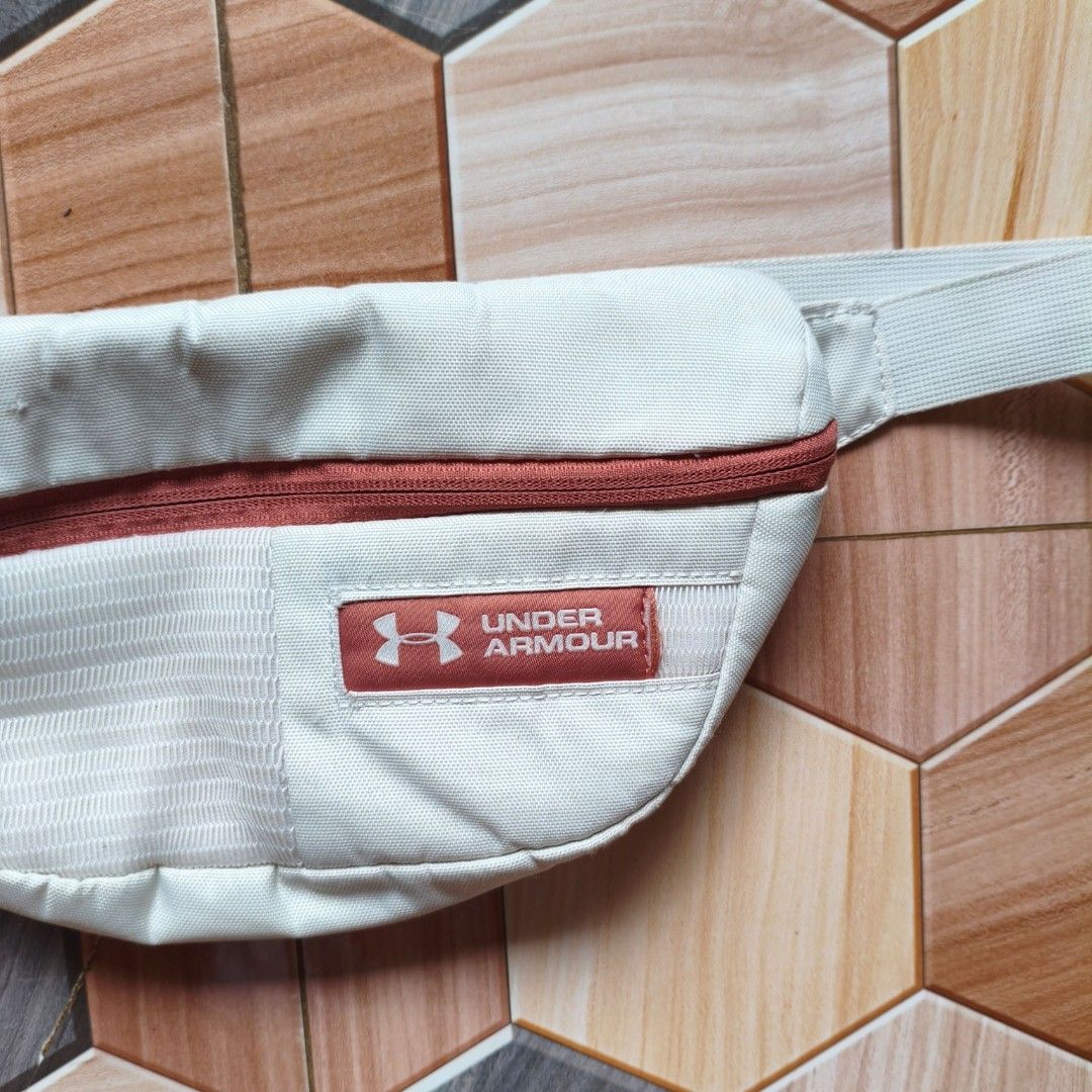 Under Armour White Fanny Pack Bum Bag (Category: Belt bags, Clutches and Pouches) located in Manila. Submitted by caps08 (Listing ID 1461594637, Image 2). Description: - White Under Armour fanny pack - Reddish-brown zipper and logo patch - Adjustable strap with buckle closure - Ideal for keeping essentials handy - Perfect for workouts or casual outings - Shows minimal signs of wear.