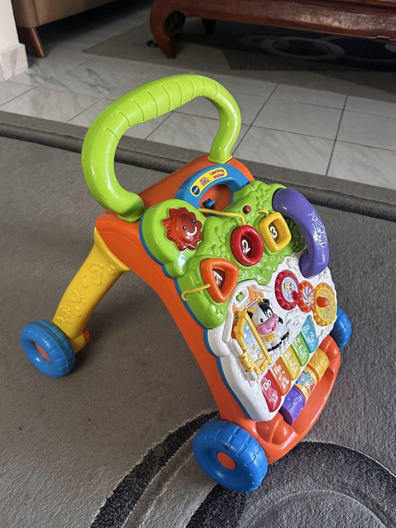 VTech Learning Walker (Category: Infant Playtime) located in Shah Alam. Submitted by bynejjaayy (Listing ID 1461740131, Image 2). Description: - VTech Learning Walker with multiple fun activities. - Features a piano keyboard, shape sorter, number buttons, and a pretend phone. - Easy-to-grip handle for little hands. - Smooth-rolling wheels designed for stability. - Perfect for encouraging baby's first steps and interactive playtime. - Bright, colo