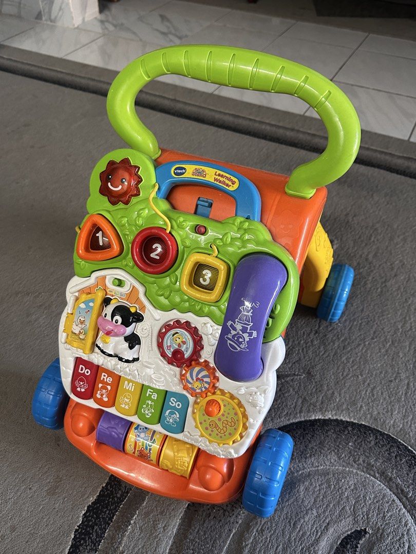 VTech Learning Walker (Category: Infant Playtime) located in Shah Alam. Submitted by bynejjaayy (Listing ID 1461740131, Image 3). Description: - VTech Learning Walker with multiple fun activities. - Features a piano keyboard, shape sorter, number buttons, and a pretend phone. - Easy-to-grip handle for little hands. - Smooth-rolling wheels designed for stability. - Perfect for encouraging baby's first steps and interactive playtime. - Bright, colo