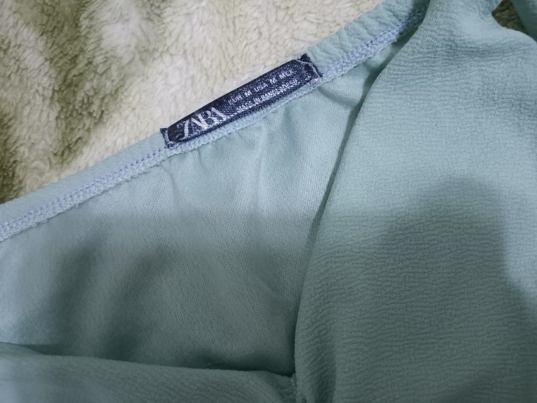 Zara Off Shoulder Ruched V-Neck Top (Category: Blouses) located in Las Pinas. Submitted by ZHOEYCLOTHING (Listing ID 1461781750, Image 2). Description: - Zara light blue off-shoulder top - Size M (estimated) - Ruched V-neck design - Billowy sleeves with elastic cuffs - Slightly textured fabric.