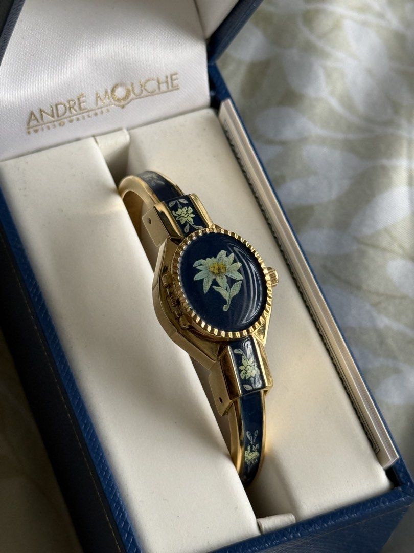 Andre Mouche Swiss Made Edelweiss Bangle Watch (Category: Women's Watches) located in Manila. Submitted by beaalipon (Listing ID 1461818496, Image 1). Description: - Authentic Andre Mouche Swiss Made watch - Elegant gold tone bangle - Dark blue enamel band with delicate edelweiss floral design - Classic white watch face with clear black numbers - Comes with original box - Includes international guarantee certificate - 14-16cm Location: BGC.