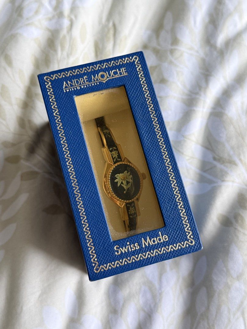 Andre Mouche Swiss Made Edelweiss Bangle Watch (Category: Women's Watches) located in Manila. Submitted by beaalipon (Listing ID 1461818496, Image 2). Description: - Authentic Andre Mouche Swiss Made watch - Elegant gold tone bangle - Dark blue enamel band with delicate edelweiss floral design - Classic white watch face with clear black numbers - Comes with original box - Includes international guarantee certificate - 14-16cm Location: BGC.