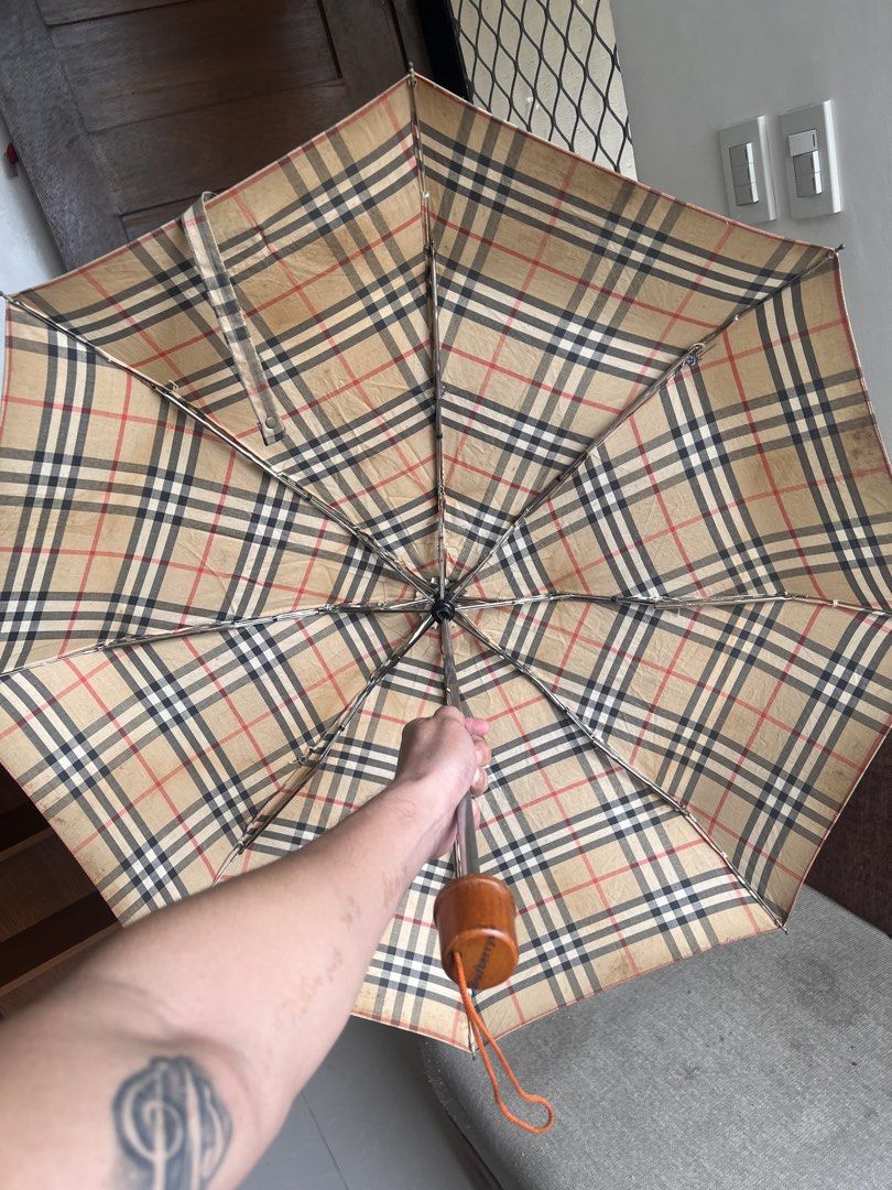 Burberry Check Folding Umbrella (Category: Umbrellas) located in San Juan, La Union. Submitted by jeggystyle (Listing ID 1461965670, Image 2). Description: - Classic Burberry check design - Folding umbrella for portability - Smooth opening and closing mechanism - Features a stylish wood-look handle - Secure button closure on the strap - Perfect for rainy weather - Shows minor signs of wear, but fully functional.