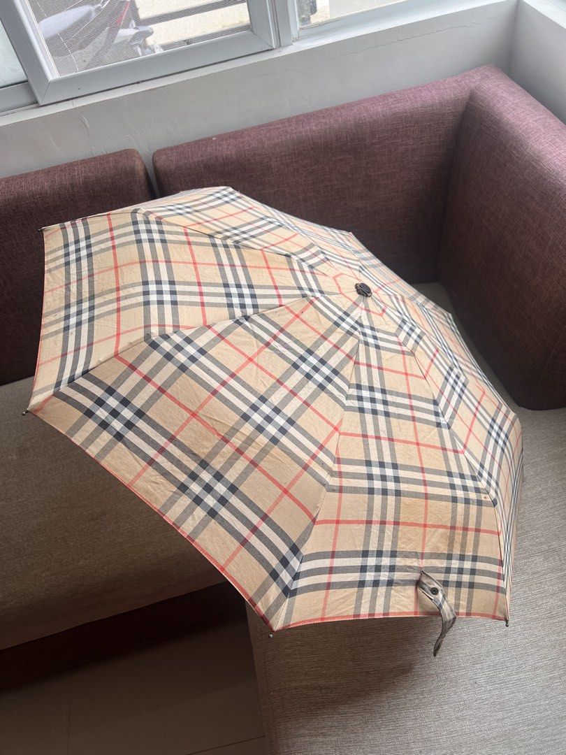Burberry Check Folding Umbrella (Category: Umbrellas) located in San Juan, La Union. Submitted by jeggystyle (Listing ID 1461965670, Image 1). Description: - Classic Burberry check design - Folding umbrella for portability - Smooth opening and closing mechanism - Features a stylish wood-look handle - Secure button closure on the strap - Perfect for rainy weather - Shows minor signs of wear, but fully functional.