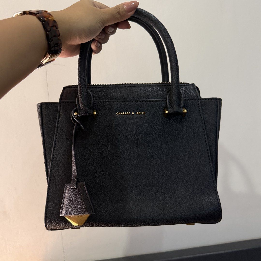 Charles & Keith Black Trapeze Tote Bag (Category: Luxury Bags & Wallets) located in Pateros City. Submitted by sachiereyes (Listing ID 1462005085, Image 1). Description: - Classic black top handle bag by Charles & Keith - Structured design with elegant gold hardware - Secure zip closure - Spacious interior compartment - Includes a detachable shoulder strap for versatile wear - Ideal for both daily use and dressing up outfits.