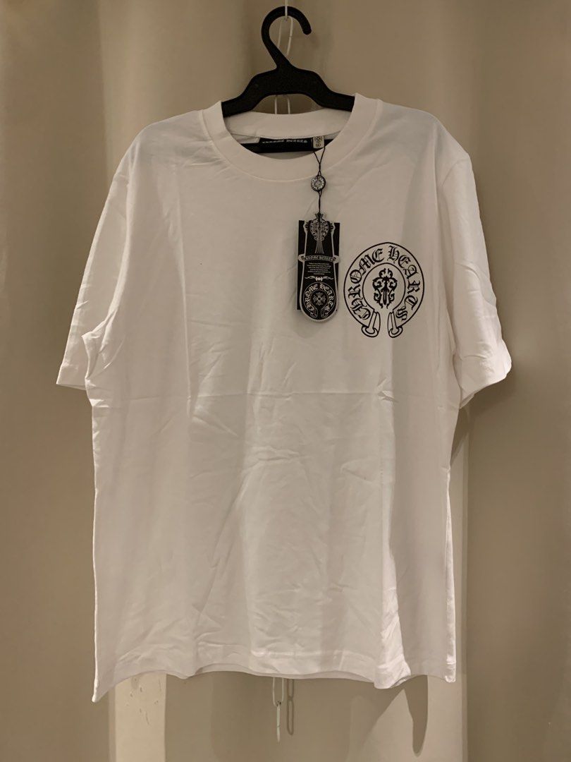 Chrome Hearts White T-Shirt (Category: Tshirts & Polo Shirts ) located in Manila. Submitted by vintaurafindsco. (Listing ID 1461829088, Image 2). Description: - Authentic White Chrome Hearts T-shirt - Features iconic dagger and scroll design on the back - Subtle Chrome Hearts logo on the front chest - Brand new with tag still attached - A must-have for any Chrome Hearts enthusiast or collector.