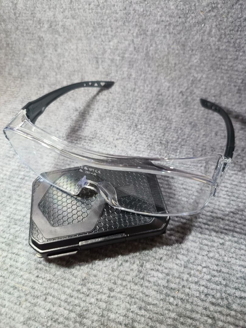 Clear Safety Glasses with Black Arms (Category: Sunglasses & Eyewear) located in San Leonardo. Submitted by burgossanleonardo.12345 (Listing ID 1461829809, Image 3). Description: - Clear safety glasses with black arms - Wrap-around design for excellent coverage - Lenses marked to meet safety standards - Protects eyes during various tasks - Lightweight and comfortable for extended wear.