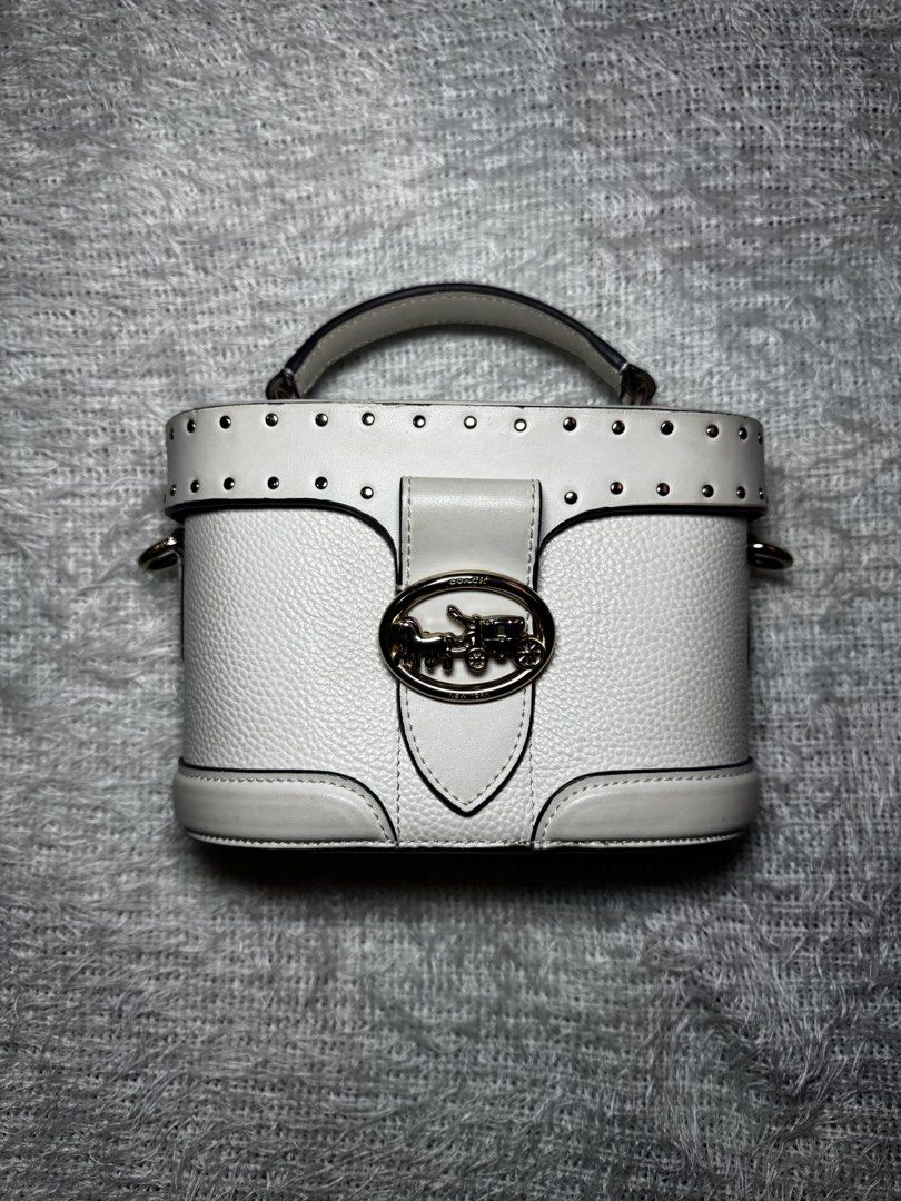 Coach White Leather Vanity Case Bag with Strap (Category: Luxury Bags & Wallets) located in Pasay City. Submitted by karenibasco (Listing ID 1461826613, Image 3). Description: - Authentic Coach white leather vanity case bag - Features signature horse and carriage logo hardware - Stylish studded detail along the top edge - Comes with a detachable crossbody strap for versatile wear - Convenient top handle for easy carrying - Ideal size for storing 