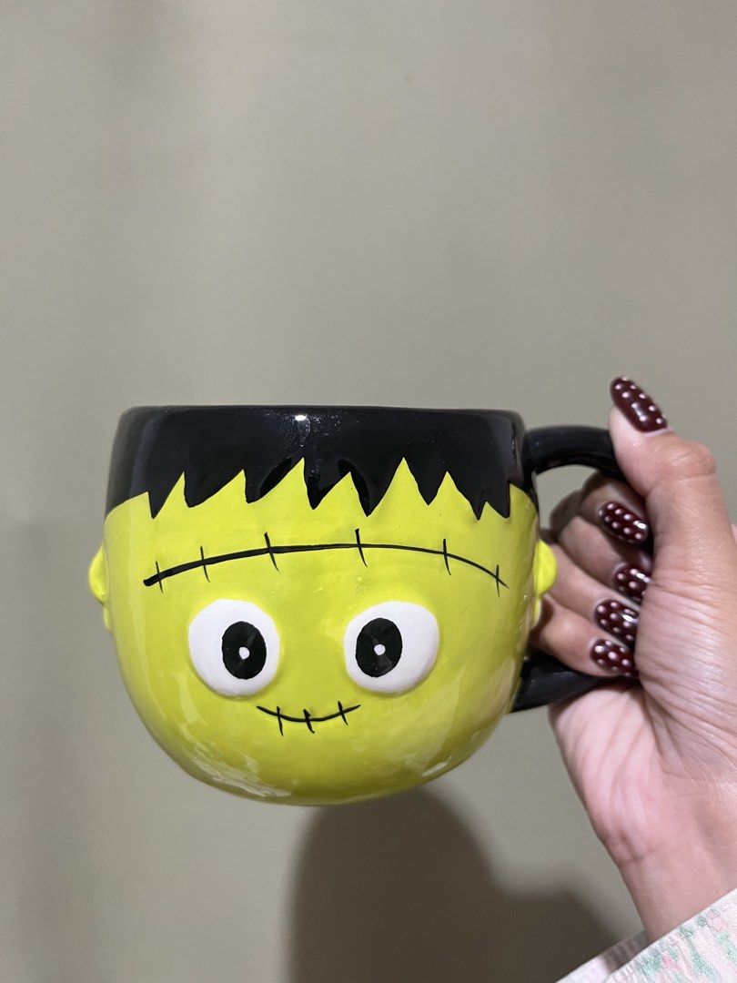 Frankenstein Halloween Ceramic Mug (Category: Coffee & Tea Tableware) located in Manila. Submitted by vaughnscloset (Listing ID 1461948829, Image 1). Description: - Fun Frankenstein mug - Bright green face with black hair and handle - Ideal for Halloween or year-round spooky vibes - Suitable for coffee, tea, or hot chocolate - Dishwasher safe (handwashing recommended for longevity) - A unique addition to your kitchenware.