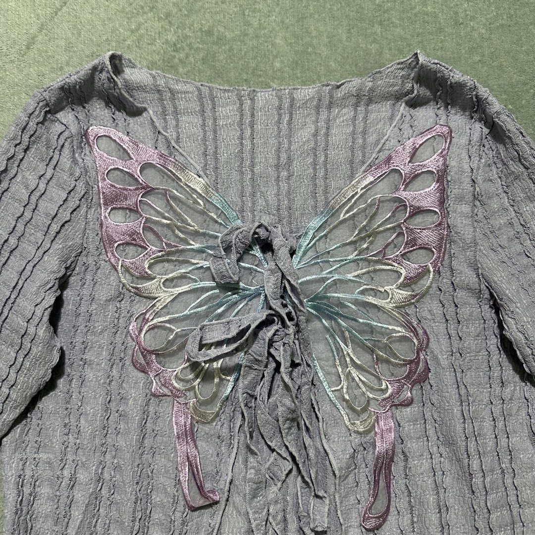 Grey Butterfly Applique Long Sleeve Top (Category: Blouses) located in Villaverde. Submitted by bakatzy_secondhand_garments (Listing ID 1461843915, Image 2). Description: - Grey textured long sleeve top - Beautiful butterfly applique with ribbon details on front - Unique bell sleeves - Cropped, asymmetrical hem - Ties at the front - Size XL.