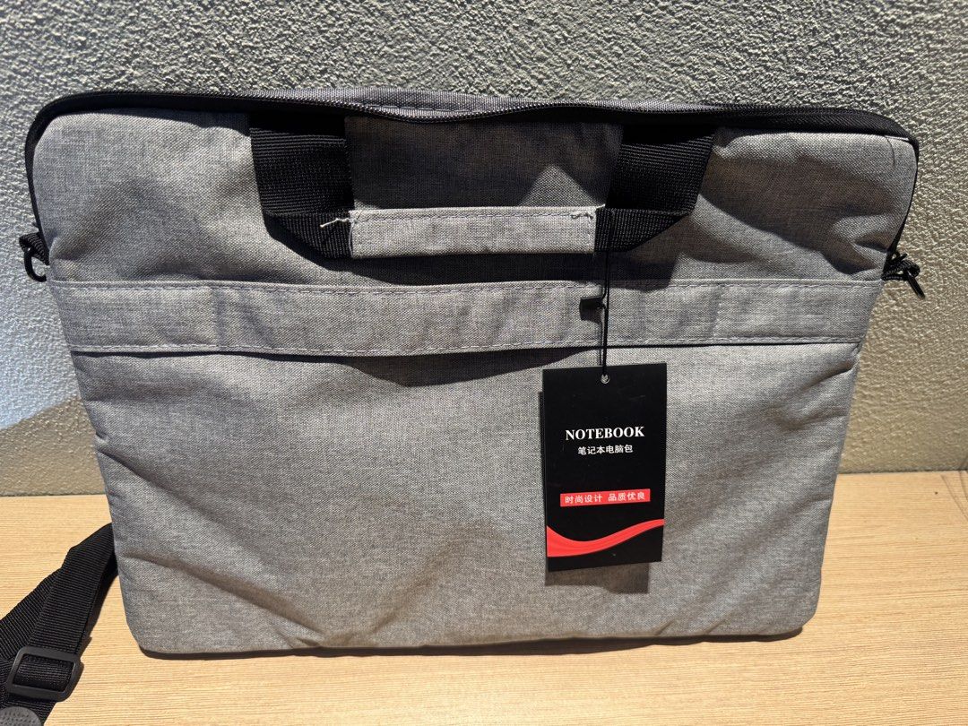 Grey Laptop Bag with Shoulder Strap (Category: Laptop Bags & Sleeves) located in Manila. Submitted by kuroshirooreo (Listing ID 1461876794, Image 2). Description: - Grey laptop bag - Features handles and a detachable shoulder strap - Lined and padded interior for protection - Tagged 'NOTEBOOK', suitable for standard laptops - Ideal for safely carrying your tech gear.