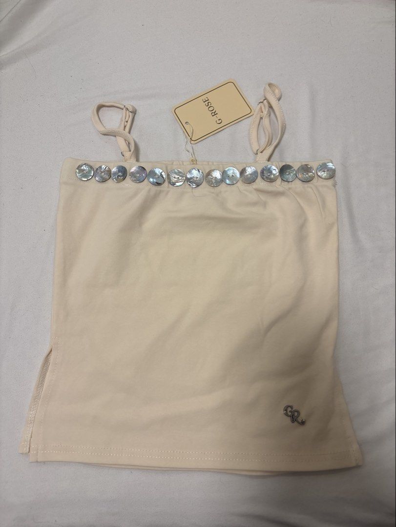 G-ROSE Cream Tank Top with Shell Buttons (Category: Sleeveless) located in Angeles City. Submitted by turonto (Listing ID 1461967528, Image 1). Description: - Cream colored tank top from G-ROSE - Features a row of shell buttons along the neckline - Adjustable spaghetti straps - Small side slits at the hem - Versatile for layering or wearing on its own.