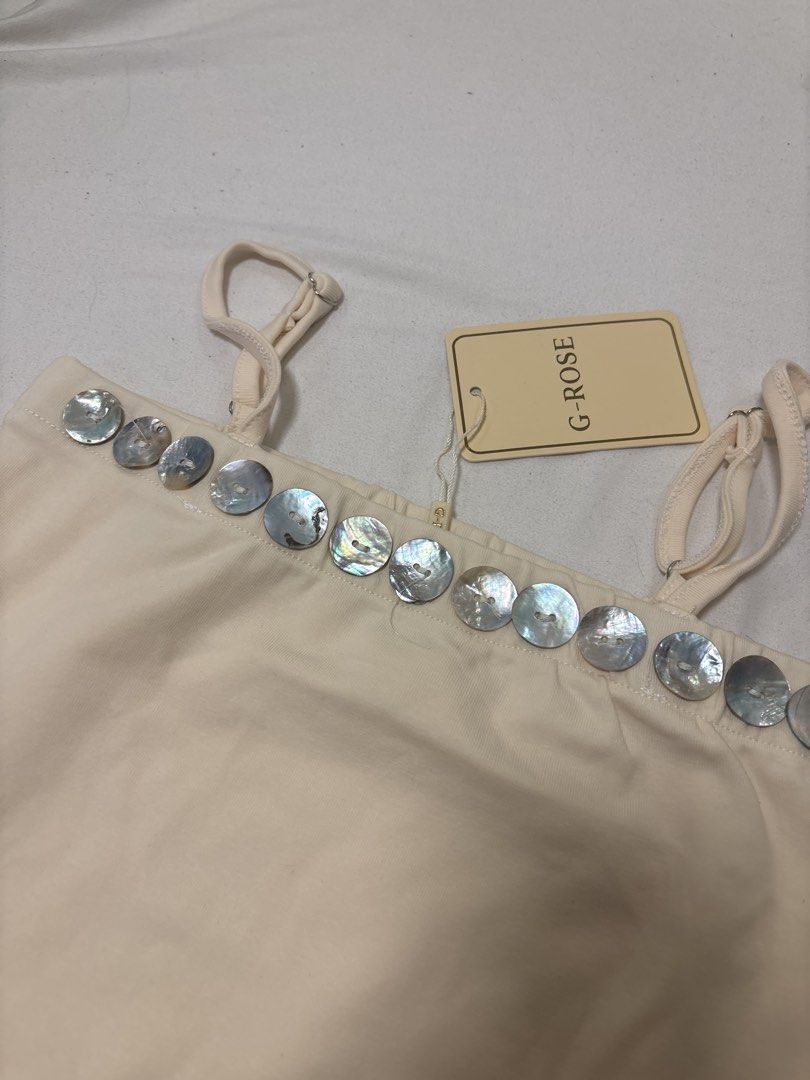 G-ROSE Cream Tank Top with Shell Buttons (Category: Sleeveless) located in Angeles City. Submitted by turonto (Listing ID 1461967528, Image 2). Description: - Cream colored tank top from G-ROSE - Features a row of shell buttons along the neckline - Adjustable spaghetti straps - Small side slits at the hem - Versatile for layering or wearing on its own.