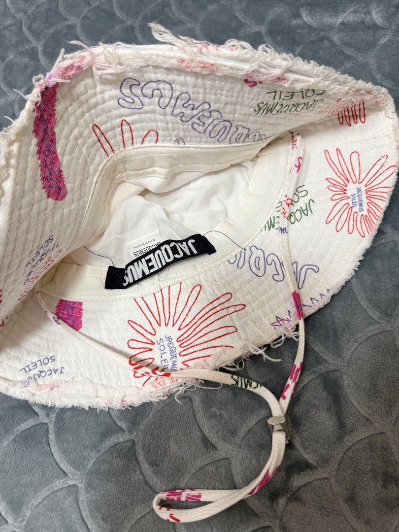 Jacquemus Soleil Bucket Hat White All Over Print (Category: Hats & Beanies) located in Tarlac. Submitted by kylienclrzbl (Listing ID 1461918002, Image 2). Description: - White bucket hat with all-over Jacquemus Soleil print - Features a frayed brim - Includes a drawstring for adjustable fit - Fun graphics all over - Ideal for sunny days and outdoor activities.