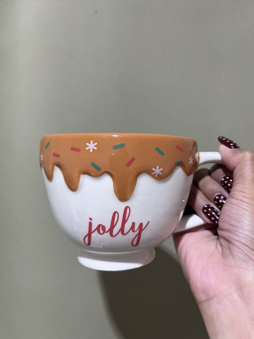 Jolly Christmas Ceramic Mug with Gingerbread Drip Design (Category: Coffee & Tea Tableware) located in Manila. Submitted by vaughnscloset (Listing ID 1461946312, Image 1). Description: - Cute white ceramic mug with 'Jolly' in red script. - Features a gingerbread drip design around the rim. - Decorated with festive sprinkles and snowflakes. - Ideal for hot cocoa or coffee during the holidays. - Makes a wonderful gift or a treat for yourself! - Cer