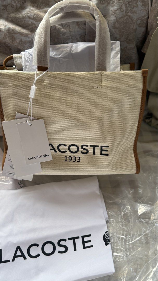 Lacoste Canvas Tote Bag with Leather Trim (Category: Tote Bags) located in Las Pinas. Submitted by tin0805 (Listing ID 1461906452, Image 1). Description: - Classic beige canvas tote from Lacoste - Brown leather trim and handles - Iconic Lacoste logo printed on the front - Interior lining with repeating Lacoste pattern - Comes with original dust bag and tags - Ideal for everyday use 📍Alabang Area .