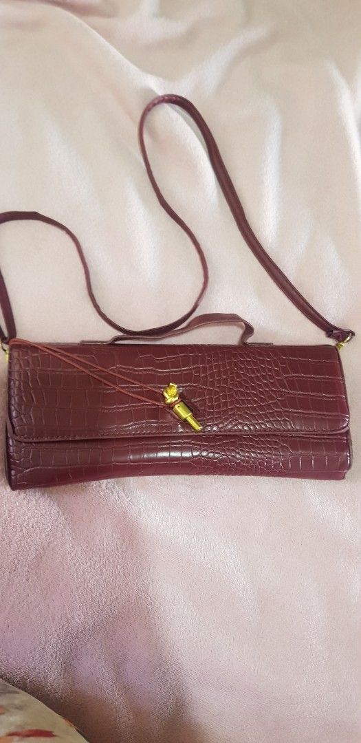 Maroon Crocodile Embossed Clutch Bag with Strap (Category: Clutches) located in Quezon City. Submitted by seventeenjeonghan (Listing ID 1461808098, Image 2). Description: - Elegant maroon clutch bag - Crocodile embossed texture - Convenient top handle - Detachable long strap for versatility - Stylish gold hardware on front closure - Lined with dark green material - Ideal for evening wear and special occasions.