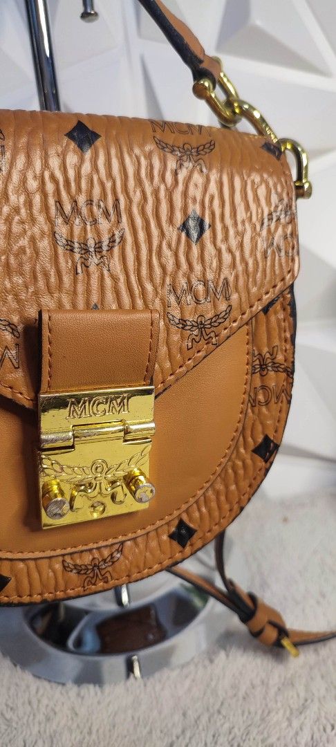MCM Visetos Saddle Bag Cognac (Category: Luxury Bags & Wallets) located in Pasig City. Submitted by xcess_baggage (Listing ID 1461888865, Image 2). Description: - Authentic brown MCM saddle bag - Signature Visetos print - Elegant gold hardware - Stylish chain strap - Interior card slots for organization - Minor wear on edges and hardware, adding character - Ideal for everyday wear.