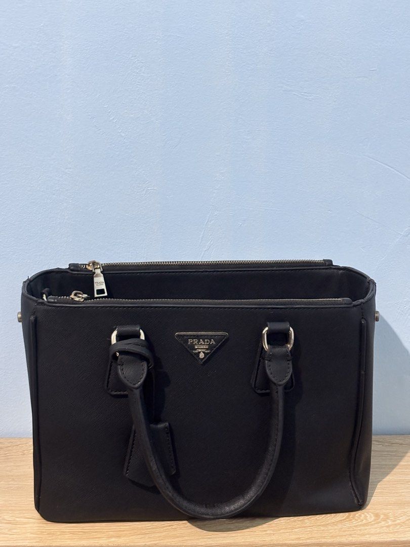 Prada Saffiano Leather Tote Bag Black (Category: Luxury Bags & Wallets) located in Manila. Submitted by maaajesstic (Listing ID 1461802628, Image 1). Description: - Classic black Prada tote bag - Genuine Saffiano leather - Elegant gold hardware details - Two comfortable top handles - Secure zip closure - Spacious interior with multiple compartments - Includes a detachable strap for versatile carrying - Ideal for daily use or travel.