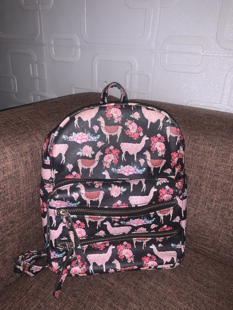 Small Mini Backpack (Category: Backpacks) located in Manila. Submitted by jei_sol (Listing ID 1461939106, Image 1). Description: UNDER1SKY ORIGINAL BACKPACK - Adorable mini backpack with a fun llama and floral print. - Features a stylish black background with vibrant pink and blue flowers. - Multiple zippered pockets on the front for easy access to essentials. - Interior is black with a small "Under One Sky" tag. - Adjustable straps for a comfort