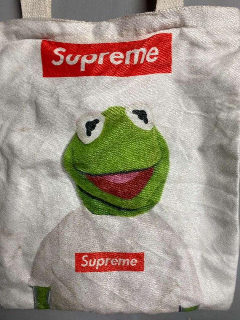 Supreme Kermit the Frog Tote Bag (Category: Sling Bags) located in Manila. Submitted by arjay_cuayzon2 (Listing ID 1461950895, Image 3). Description: - White canvas tote bag with Kermit the Frog graphic - Features two Supreme box logos - Magnetic snap closure - Minor stains visible on fabric - Ideal for everyday use.