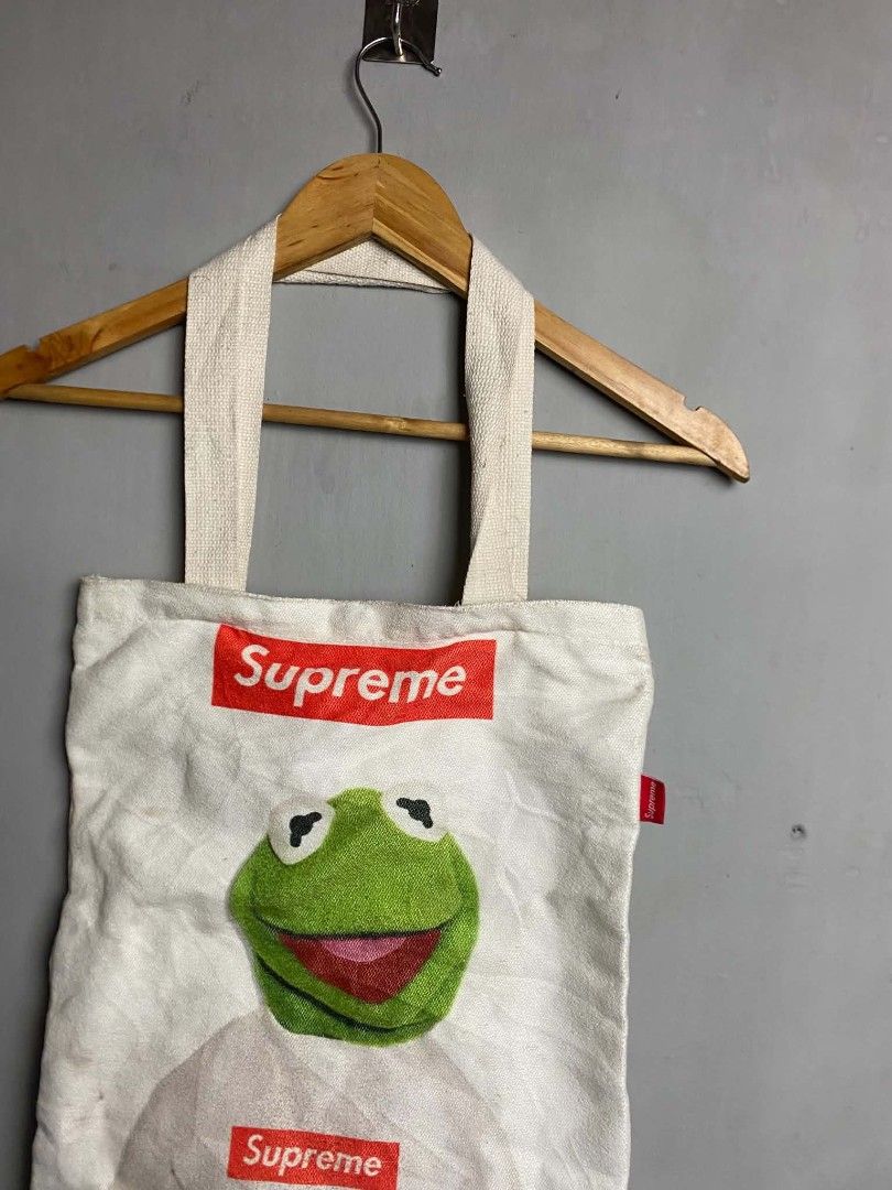 Supreme Kermit the Frog Tote Bag (Category: Sling Bags) located in Manila. Submitted by arjay_cuayzon2 (Listing ID 1461950895, Image 2). Description: - White canvas tote bag with Kermit the Frog graphic - Features two Supreme box logos - Magnetic snap closure - Minor stains visible on fabric - Ideal for everyday use.