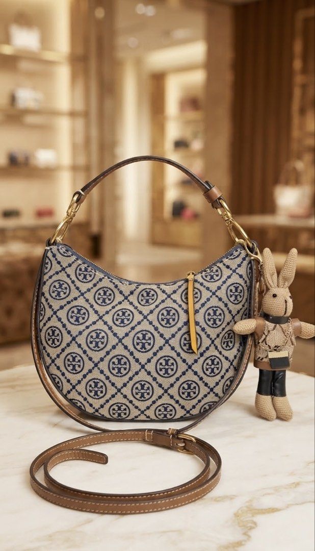Tory Burch T monogram crescent bag in navy jacquard (Category: Luxury Bags & Wallets) located in Cebu City. Submitted by forless.ph (Listing ID 1461914039, Image 1). Description: - Authentic Tory Burch shoulder bag - Classic monogram print - Adjustable leather strap - Secure zip closure - Includes a cute bunny charm - Versatile for everyday or evening wear - Genuine leather trim and strap.