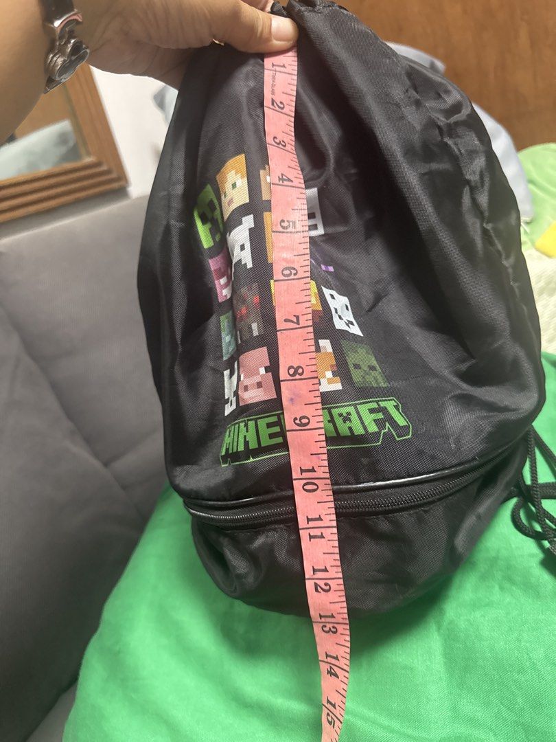 2027 Minecraft Drawstring Bag with Zippered Bottom (Category: Backpacks) located in Silang. Submitted by sari2bilina (Listing ID 1462145592, Image 2). Description: - Black drawstring bag with a fun Minecraft character print. - Features a main compartment that closes with a drawstring. - Includes a convenient zippered compartment at the bottom for extra storage. - Ideal for gym, school, or travel. - Measures approximately 15 inches tall. - A fanta