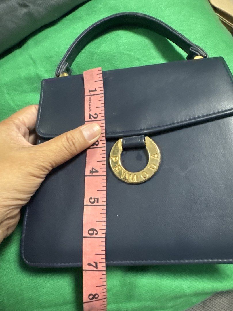2027 PRIMOD A Navy Blue Leather Handbag (Category: Luxury Bags & Wallets) located in Silang. Submitted by sari2bilina (Listing ID 1462148617, Image 2). Description: - Navy blue leather handbag - Gold ring detail with 'PRIMOD A' embossed on front - Top handle - Clean interior - Approx. 8" tall x 6" wide - Versatile for everyday or special occasions.