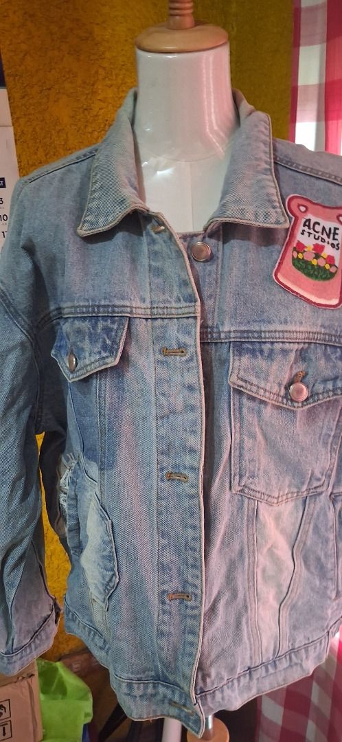 Acne Studios Denim Jacket with Embroidered Back (Category: Coats, Jackets and Outerwear) located in Manila. Submitted by katkween23 (Listing ID 1462065454, Image 2). Description: - Light wash denim jacket - Embroidered 'Solemnity' graphic on the back - Cute 'Acne Studios' patch on the front pocket - Distressed details on pockets and hem - Button-up front with chest pockets - Ideal for layering.