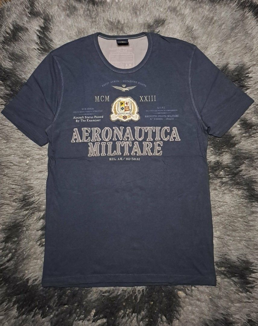 Aeronautica Militare (Category: Tshirts & Polo Shirts ) located in Manila. Submitted by yaseen__73 (Listing ID 1462204704, Image 1). Description: Aeronautica Militare crew-neck T-shirt in navy blue. It features stylized graphics inspired by the Italian Air Force, including military emblems, Roman numerals, and aviation text overlays. Wearing Size : M - L Dimensions : See Photo Color Rate : 10/10 Flawless Brand New Condition - P R E O W N E D MOP 