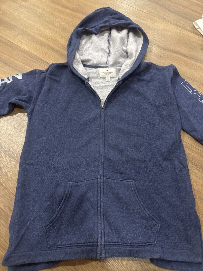 American Eagle Zip-Up Hoodie (Category: Coats, Jackets and Outerwear) located in Makati City. Submitted by curatedclosetco (Listing ID 1462157966, Image 1). Description: - Navy blue zip-up hoodie from American Eagle. - "AMERICAN" text on left sleeve. - "EAGLE 1977" text on right sleeve. - Front pocket for convenience. - Comfortable hood. - Made from soft material, perfect for casual outings..