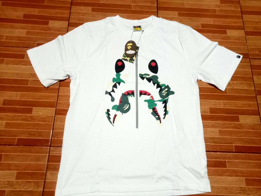 BAPE White Shark Camo Zip Tee (Category: Tshirts & Polo Shirts ) located in Manila. Submitted by jed_vilma123 (Listing ID 1462137318, Image 1). Description: - White BAPE T-shirt - Iconic shark camo graphic - Zip detail down the front - BAPE logo patch on the sleeve - Perfect for streetwear enthusiasts.