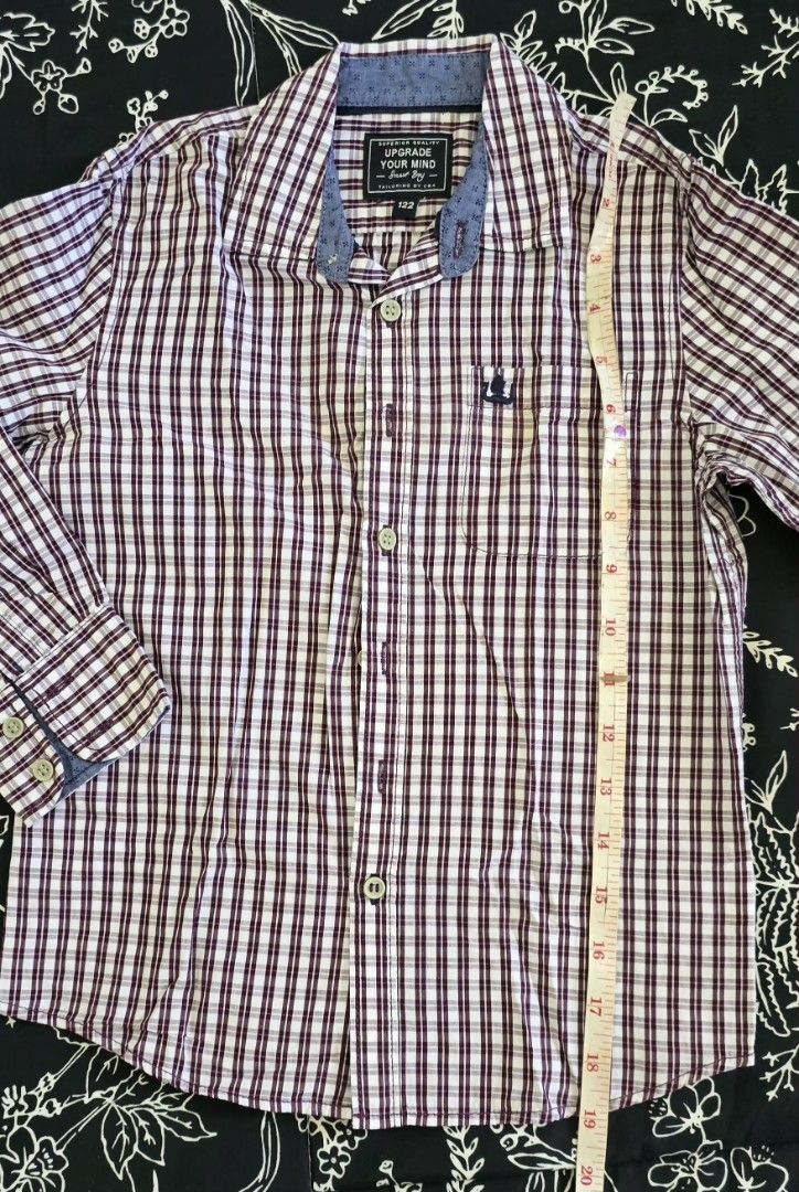Boys Plaid Button-Up Shirt (Category: Babies & Kids Fashion) located in Calamba. Submitted by _arar_ (Listing ID 1462060288, Image 3). Description: - Boys long-sleeved button-up shirt - Classic maroon and white plaid pattern - Small embroidered anchor logo on chest pocket - Contrasting blue denim-like collar fabric - Size 130 - Versatile for casual or dressy occasions.