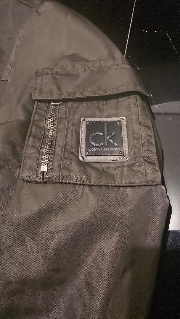 Calvin Klein Jeans Olive Green Bomber Jacket (Category: Coats, Jackets and Outerwear) located in Quezon City. Submitted by ShoesManila (Listing ID 1462089715, Image 2). Description: Width 24 Length 27 Arm length 26 CK original Condition: Excellent Color rate: 10/10 - Olive green bomber jacket from Calvin Klein Jeans - Quilted lining for warmth - Buttoned pockets for secure storage - Signature CK Jeans patch on the sleeve Ready to ship No COD Loca