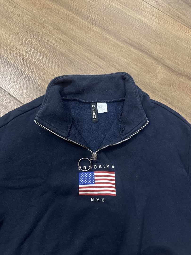 Divided Navy Brooklyn NYC Flag Half Zip Sweatshirt (Category: Longsleeves) located in Makati City. Submitted by curatedclosetco (Listing ID 1462155706, Image 1). Description: - Navy blue cropped sweatshirt from Divided - Features a half-zip neckline with a ring pull - Front graphic: Brooklyn NYC text with an American flag design - Cropped style, ideal for casual wear.
