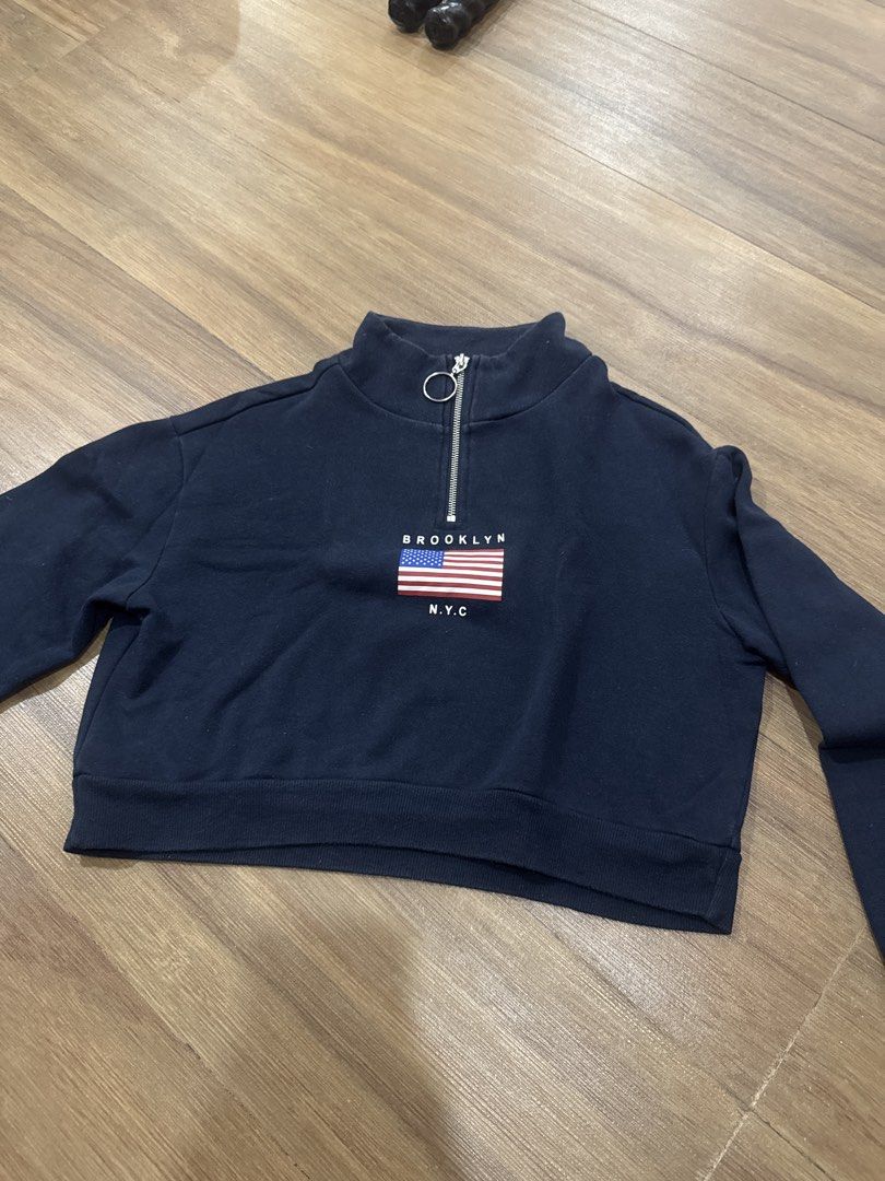 Divided Navy Brooklyn NYC Flag Half Zip Sweatshirt (Category: Longsleeves) located in Makati City. Submitted by curatedclosetco (Listing ID 1462155706, Image 2). Description: - Navy blue cropped sweatshirt from Divided - Features a half-zip neckline with a ring pull - Front graphic: Brooklyn NYC text with an American flag design - Cropped style, ideal for casual wear.