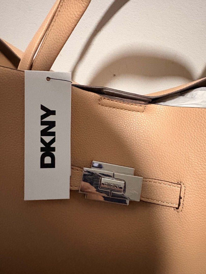 DKNY TOTE BAG (Category: Tote Bags) located in Quezon City. Submitted by pr0duct_paradize (Listing ID 1462083757, Image 2). Description: FOR SALE! BRAND NEW ORIGINAL PRICE 13k SELLING IT FOR 9k BINILI SA IRELAND CHECK THE PRICE AND TAG ON PHOTOS POSTED Original cappuccino-colored DKNY tote bag featuring a polished silver-tone buckle closure on the front. HELPING A FRIEND LOCATION: NOVALICHES QC PICK UP OR BOOK AN APP.
