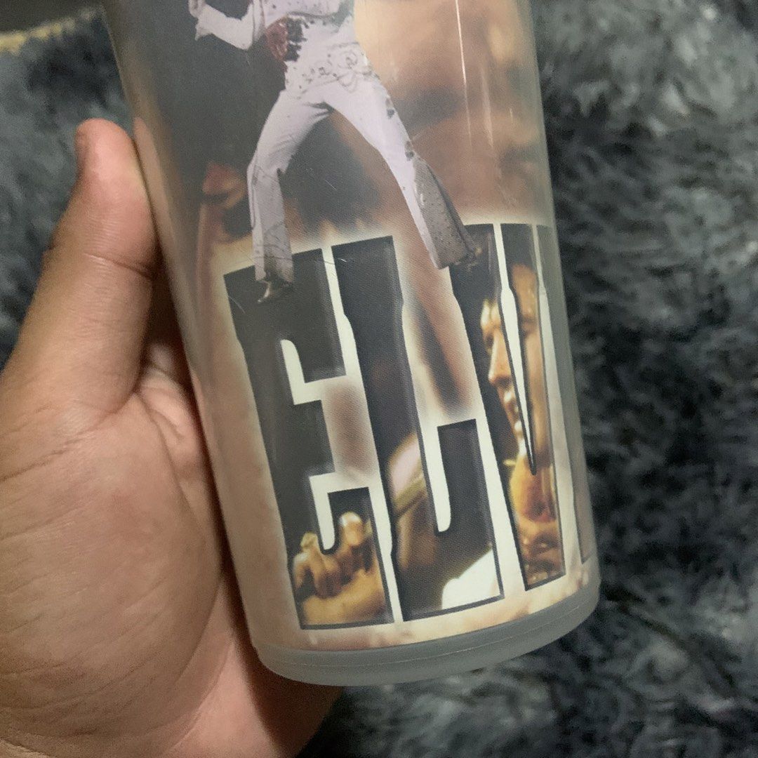 Elvis Presley Tumbler Cup (Category: Water Bottles & Tumblers) located in Compostela. Submitted by anyastark (Listing ID 1462123611, Image 2). Description: - Vintage Elvis Presley tumbler - Features iconic images of the King of Rock and Roll - Comes with a black lid - Great for any Elvis fan's collection - Ideal for your favorite beverages.