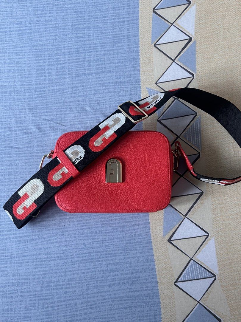 Furla Sleek Mini Camera Case Fuoco/Toni Nero One Size (Category: Luxury Bags & Wallets) located in Manila. Submitted by declutwithmj (Listing ID 1462087277, Image 2). Description: - Authentic Furla red leather crossbody bag - Features a secure gold lock closure - Adjustable black strap with repeating Furla logos - Versatile for everyday wear or evening outings - Comes with original Furla card.