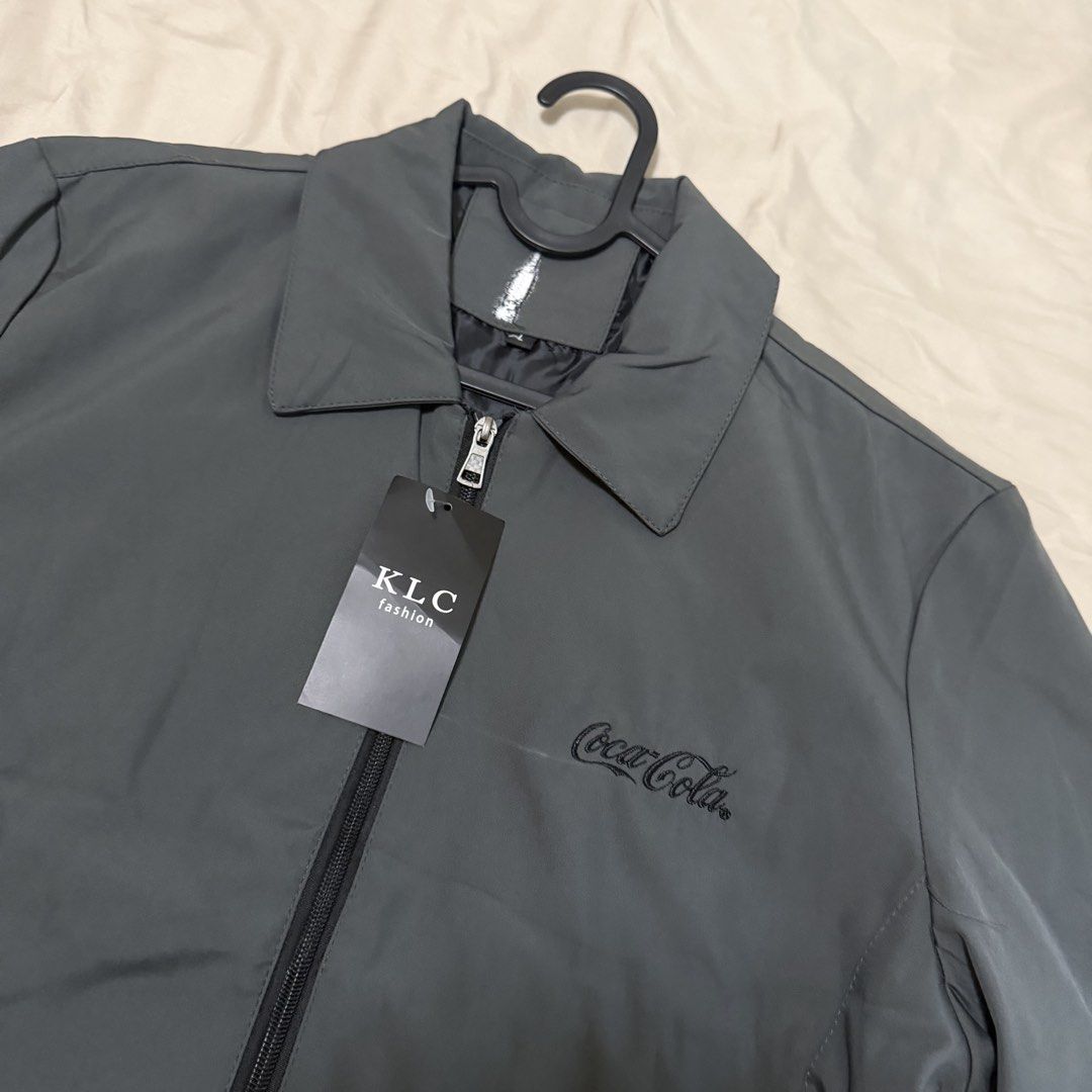 HIGH QUALITY NEW Coca-Cola Grey Zip-Up Jacket (Category: Coats, Jackets and Outerwear) located in Taguig. Submitted by shopailynht (Listing ID 1462123967, Image 2). Description: - Grey jacket with iconic Coca-Cola branding. - Features a zip-up front and a classic collar. - Two convenient buttoned pockets on the front. - Stylish buttoned cuffs for a tailored look. - Swipe to see measurements - New never used .