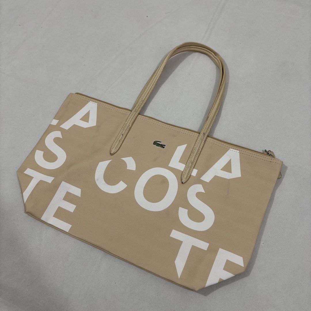 Lacoste Beige Tote Bag with Large Logo Print (Category: Tote Bags) located in Cavite. Submitted by itsayaaa (Listing ID 1462093261, Image 2). Description: - Beige Lacoste tote bag - All-over white logo print - Zippered closure - Two comfortable handles - Multiple interior compartments - Includes a small zippered pouch - Interior lining with repeated Lacoste logo - Ideal for everyday use.