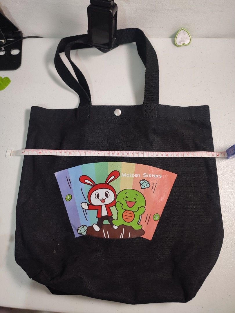 Maizen Sisters Black Canvas Tote Bag (Category: Tote Bags) located in Marikina City. Submitted by surplusbuffet (Listing ID 1462203740, Image 2). Description: - Black canvas tote bag featuring Maizen Sisters characters. - Adorable rainbow fan design on the front. - Secure button closure at the top. - Sturdy handles for comfortable carrying. - Ideal for books, groceries, or daily essentials. - Approximate dimensions: 38cm (height) x 35cm (width)..