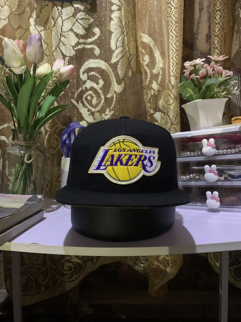 Mitchell & Ness Los Angeles Lakers Snapback Cap (Category: Caps & Hats) located in Quezon. Submitted by ken2x_thrift (Listing ID 1462081651, Image 1). Description: - Black snapback cap - Features the iconic Los Angeles Lakers logo - Stylish gold brim - Mitchell & Ness branding inside and on the back - Adjustable strap for a custom fit - Perfect for any Lakers fan!.