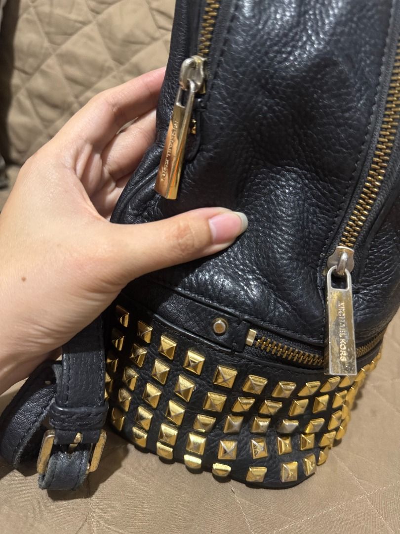 MK RHEA (MEDIUM SIZE) (Category: Backpacks) located in San Pablo. Submitted by calmhawk.60c993 (Listing ID 1462091902, Image 2). Description: The item appears to be a black pebbled leather Michael Kors Rhea Medium Studded Backpack featuring striking gold pyramid studs along the front pocket. Slightly used kasya po macbook neo since med size po siya... kulang lang po ng dalawang studd sa gilid pls see the last pics...