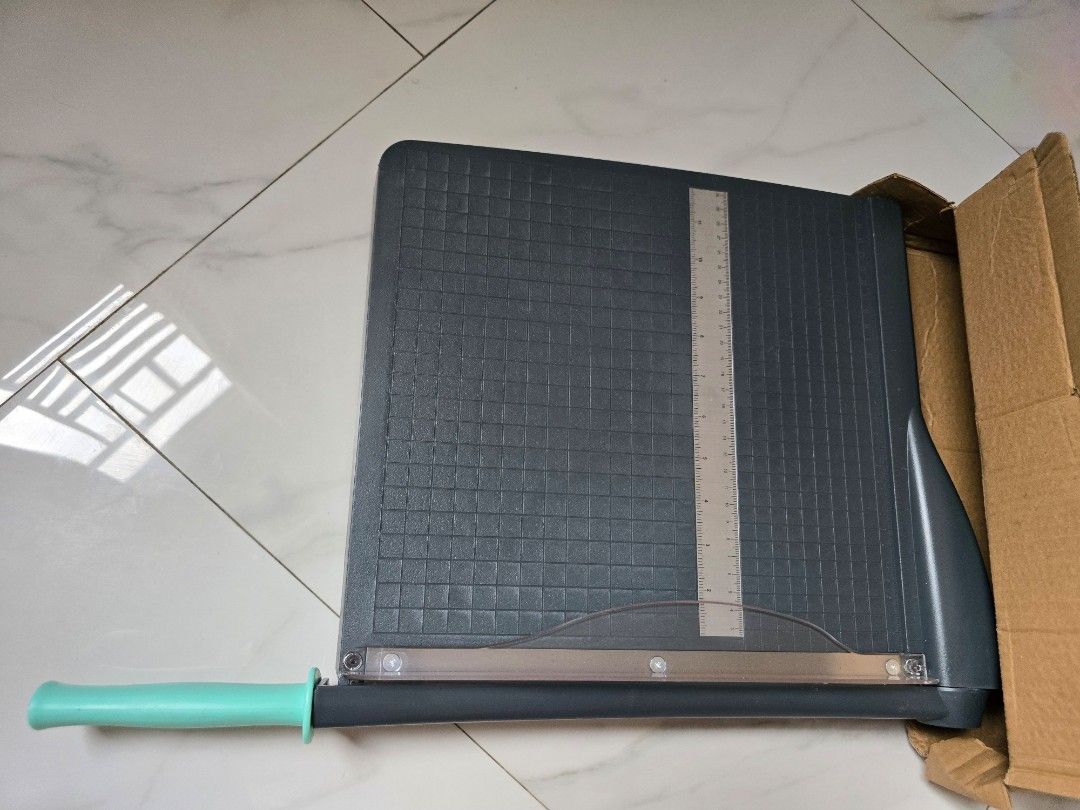 Paper Trimmer Guillotine with Ruler (Category: Craft Supplies & Tools) located in Taguig. Submitted by thriftzzzy (Listing ID 1462096141, Image 1). Description: - Grey paper trimmer with a light blue handle. - Built-in ruler marked in inches and centimeters. - Grid lines on the cutting surface for precise alignment. - Sturdy base with non-slip feet for stability. - Ideal for crafting, scrapbooking, and office tasks. - Delivers clean, precise cuts