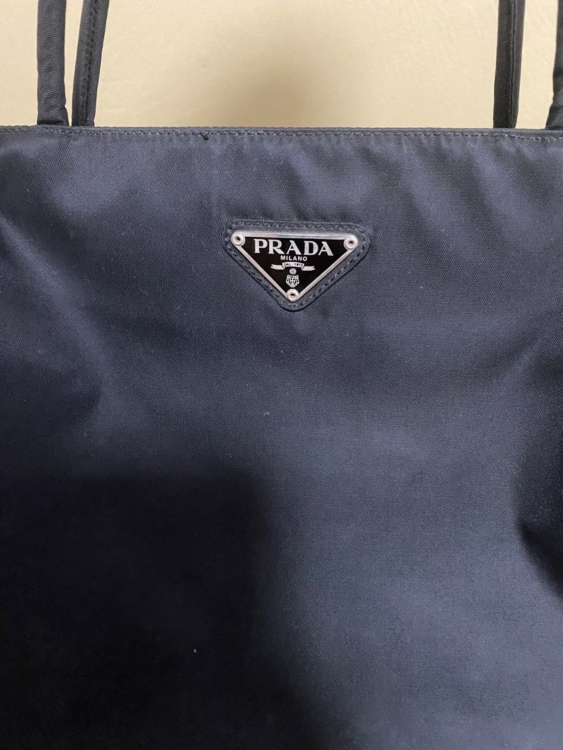 Prada Nylon Tote Bag (Category: Luxury Bags & Wallets) located in Agdangan. Submitted by aikara683 (Listing ID 1462053554, Image 2). Description: - Classic navy blue Prada tote bag - Made from durable nylon - Iconic Prada triangle logo on the front - Interior zippered pocket - Great for everyday use - Minor marks on exterior (please check photos).